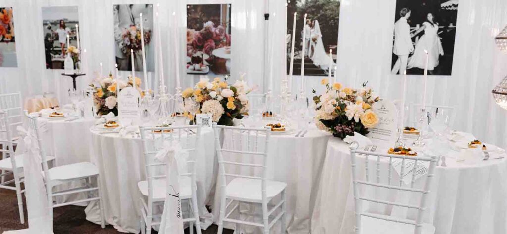 Elegant wedding reception table with white linens, tall candles, and peach-pink floral centerpieces.