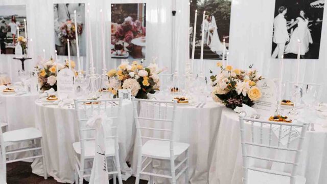 Elegant wedding reception table with white linens, tall candles, and peach-pink floral centerpieces.