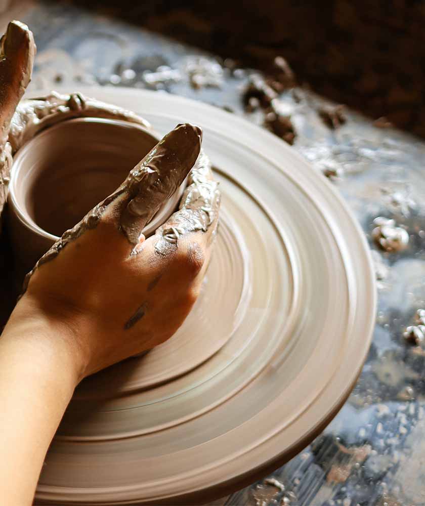 Hands covered in wet clay shaping a pot on a spinning pottery wheel.