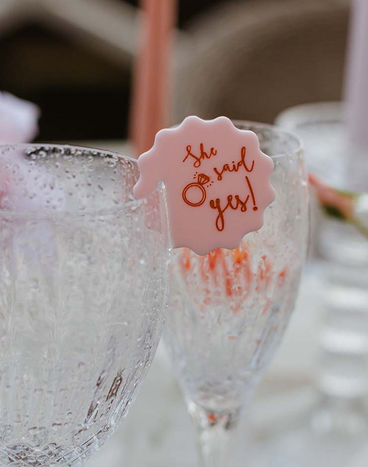1 - I do I do Gippsland Pink seal on champagne glass reads "she said yes!" during a toast at a celebration.