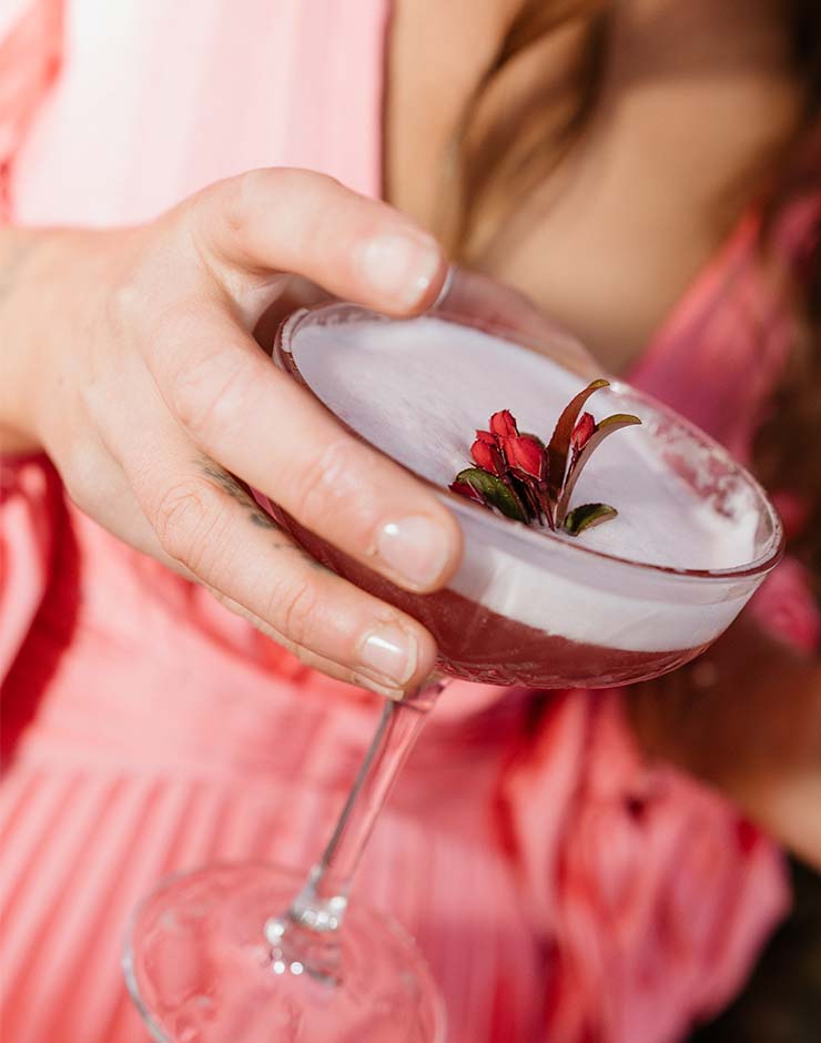 1 - I do I do Gippsland Close-up of a hand holding a pink cocktail in a coupe glass topped with foam and a red berry garnish.