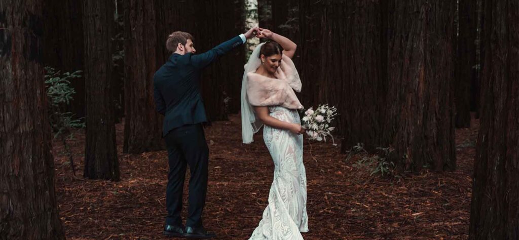 Bride and groom dancing in a forest; the groom lifts the bride's hand for a twirl.