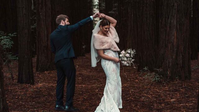 Bride and groom dancing in a forest; the groom lifts the bride's hand for a twirl.