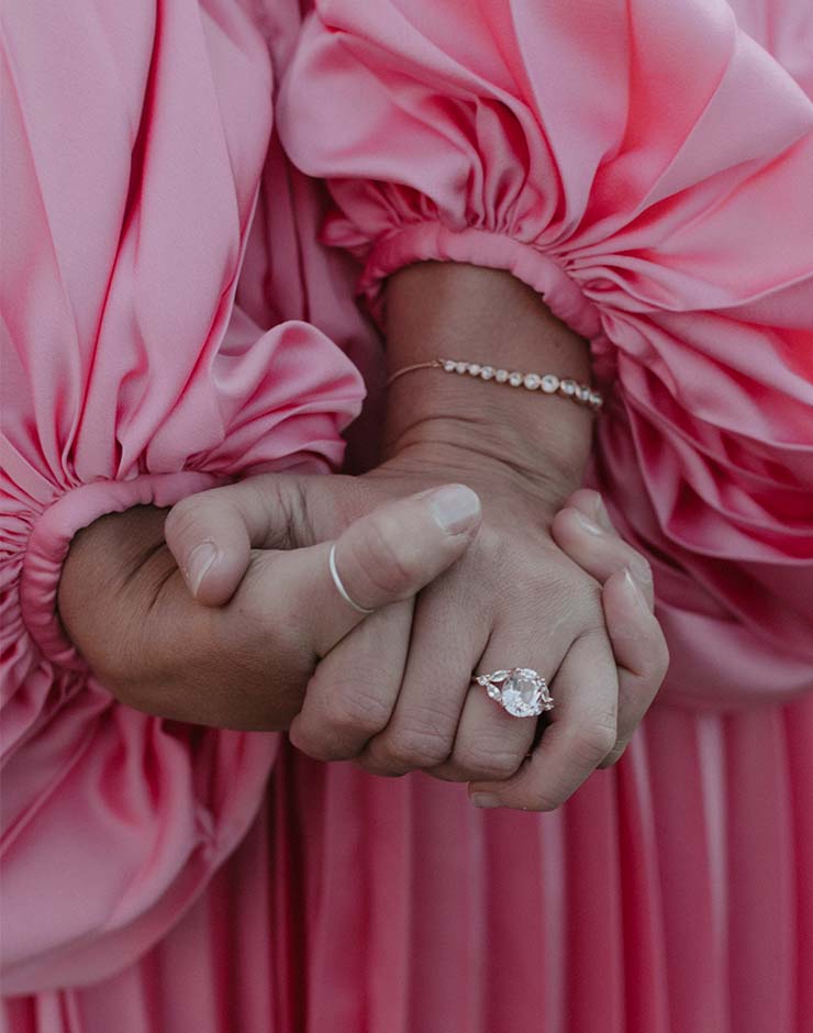 2 - I do I do Gippsland Close-up of two hands clasped together; one shows a diamond engagement ring, pink satin sleeves in the background.