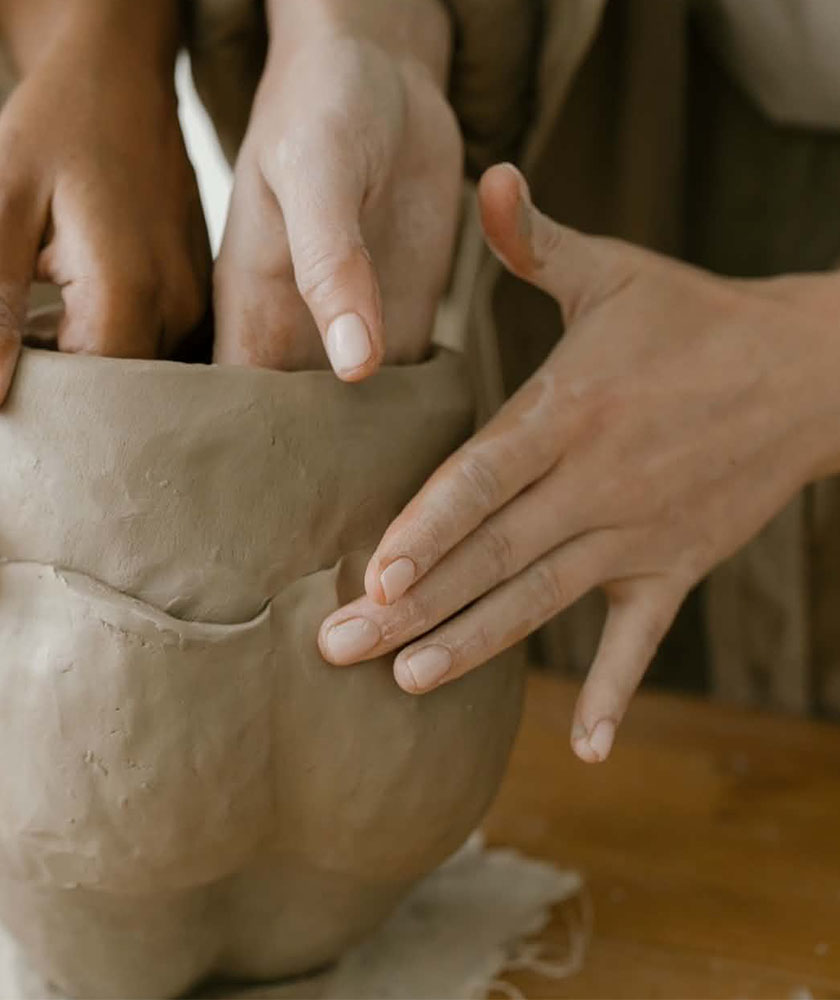 Close-up of hands shaping a clay pot, smoothing the rim on a wooden work surface.