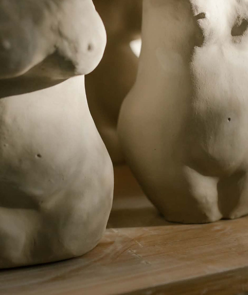 Close-up of two beige ceramic sculptures resembling abstract human torsos facing away, on a wooden surface.