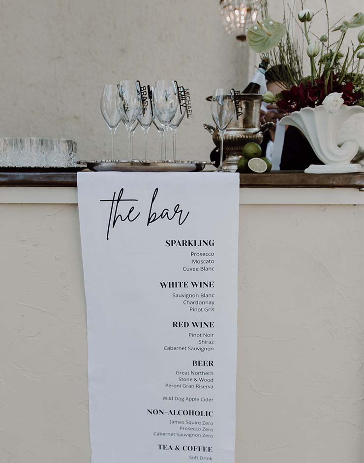 3 - I do I do Gippsland Bar counter with a hanging menu listing Sparkling, White Wine, Red Wine, Beer, and Non-Alcoholic options, and a row of empty wine glasses on a tray nearby.