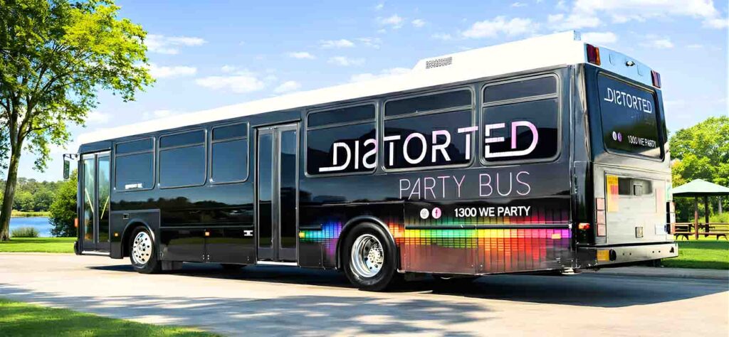 Black party bus with rainbow light-strip graphics and large white lettering, parked on a sunny driveway beside trees and a lake.