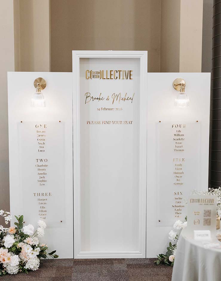 7 - I do I do Gippsland White triptych wedding seating chart with gold text; center panel lists names Brooke & Michael and date, floral arrangements at base.