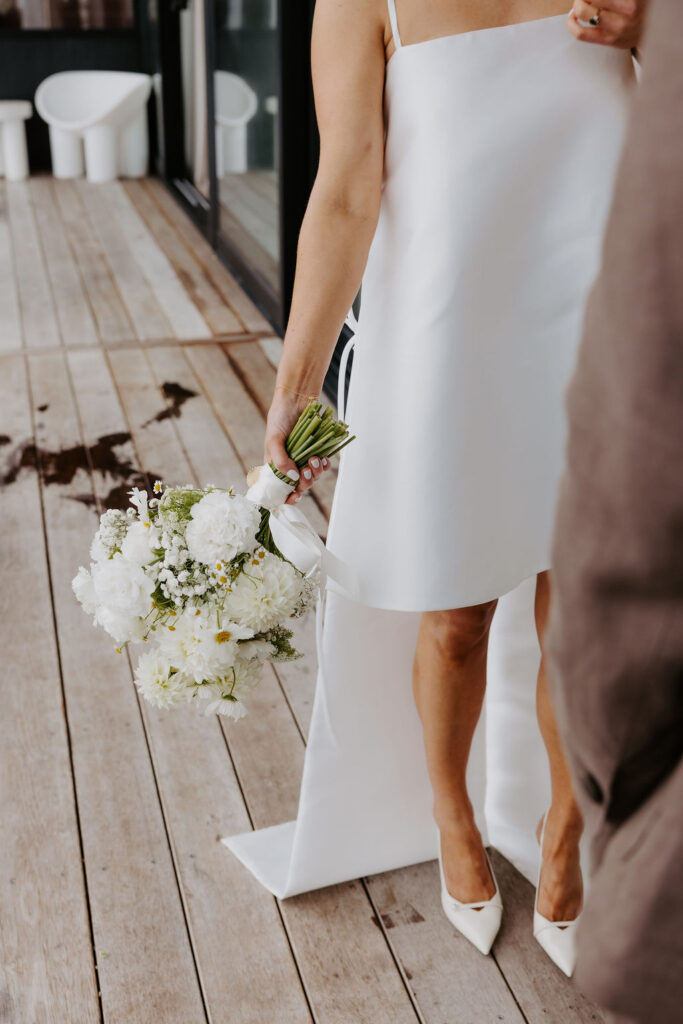Bride in a white dress holding a white bouquet on a wooden deck.