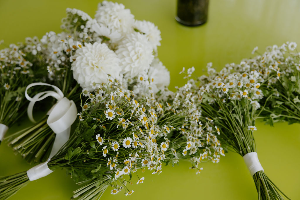 Two bouquets of white daisies and white chrysanthemums tied with white ribbons sit on a bright green table surface.
