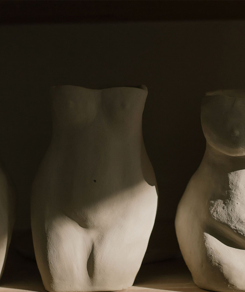 Two white plaster torso sculptures on a shelf, lit from the side in dim lighting.