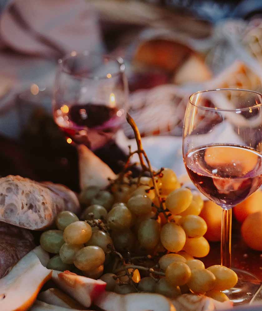 Wine glasses and a grape cluster on a charcuterie board with bread and cheese.