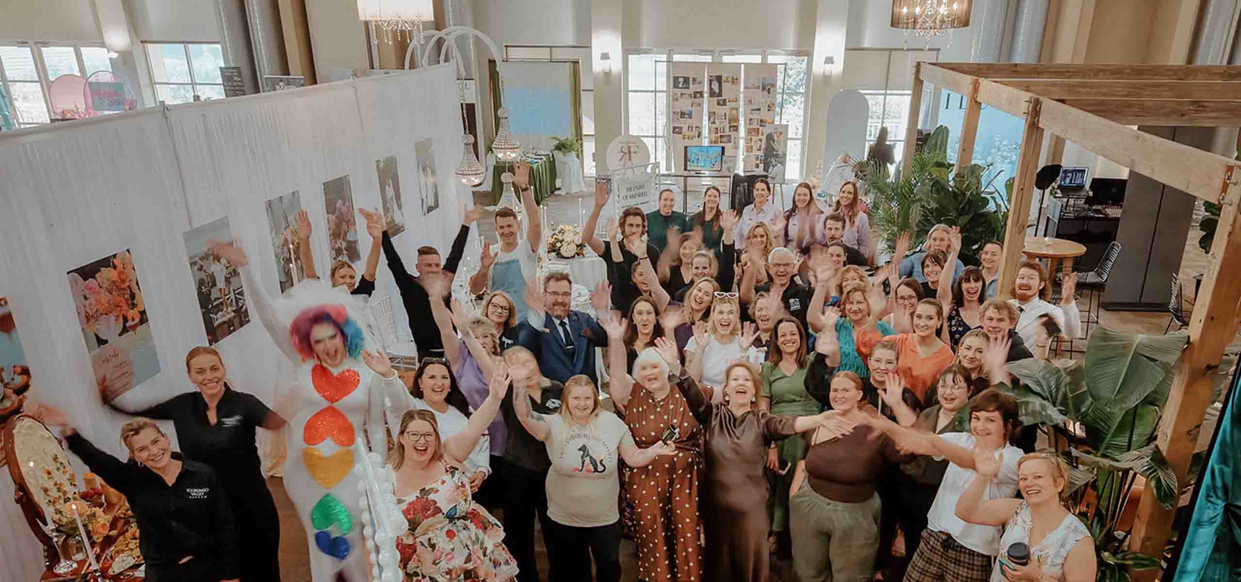 Large group of people at an indoor event, many raising hands and smiling in celebration.