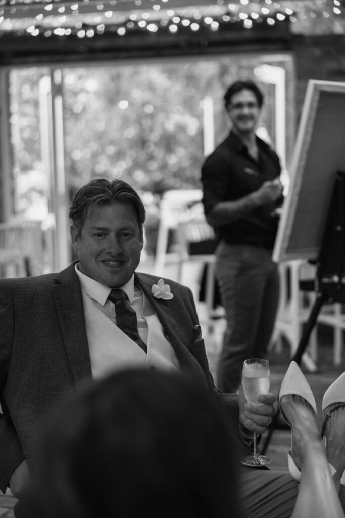 219A8693 1 | I do I do Gippsland Smiling man in a suit raises a glass at a toast during a formal event, with guests in the background.