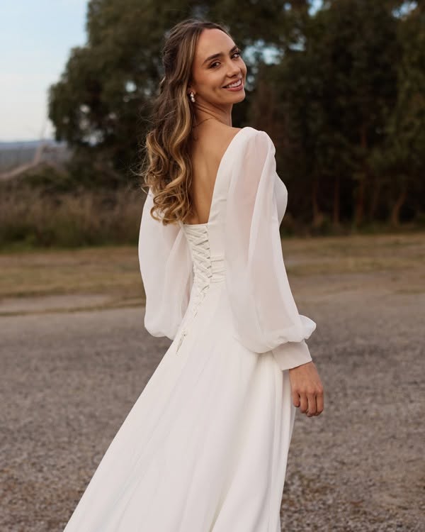 491934108_1087661846716366_8351883828688071011_n - I do I do Gippsland Woman in a white, back-laced gown outdoors, smiling while looking over her shoulder.
