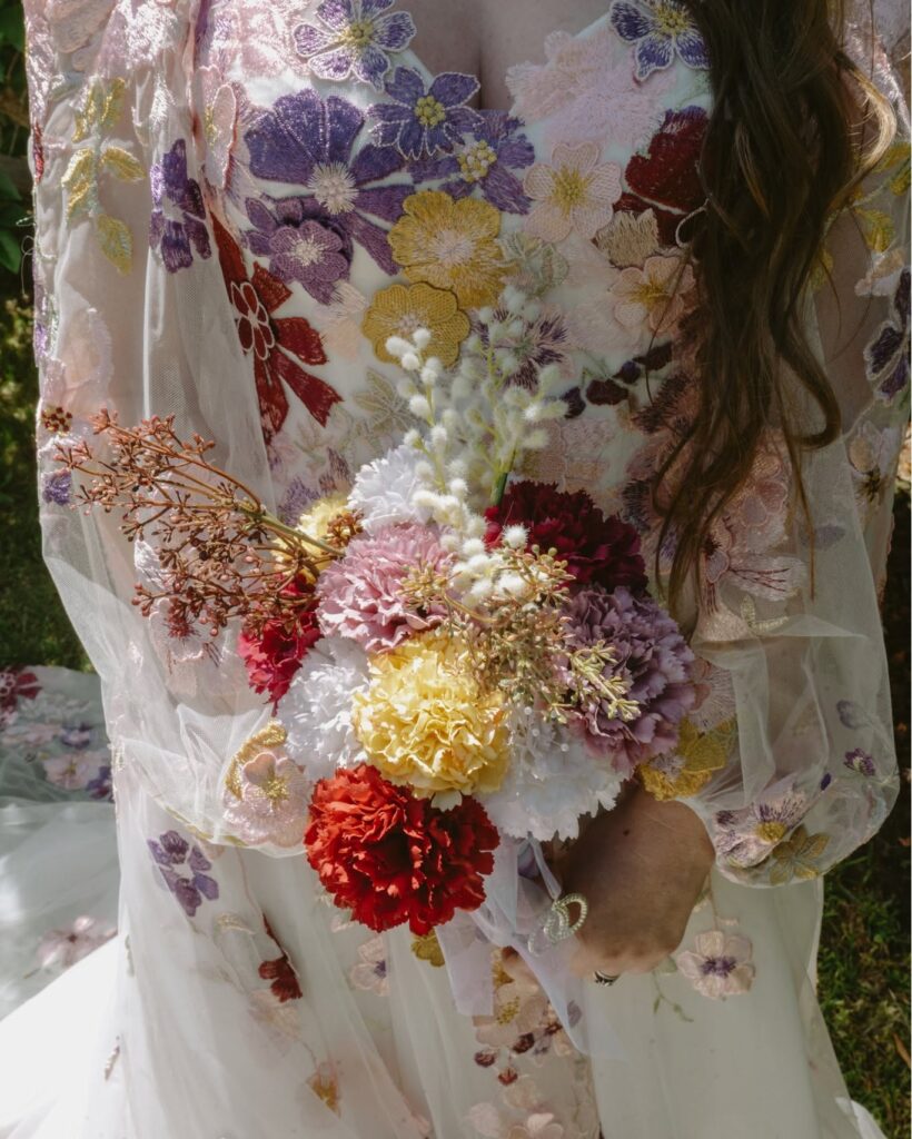 579007478_1256569393158943_7721071023672522165_n - I do I do Gippsland Close-up of a person in a sheer floral-embroidered dress holding a pastel bouquet of flowers.