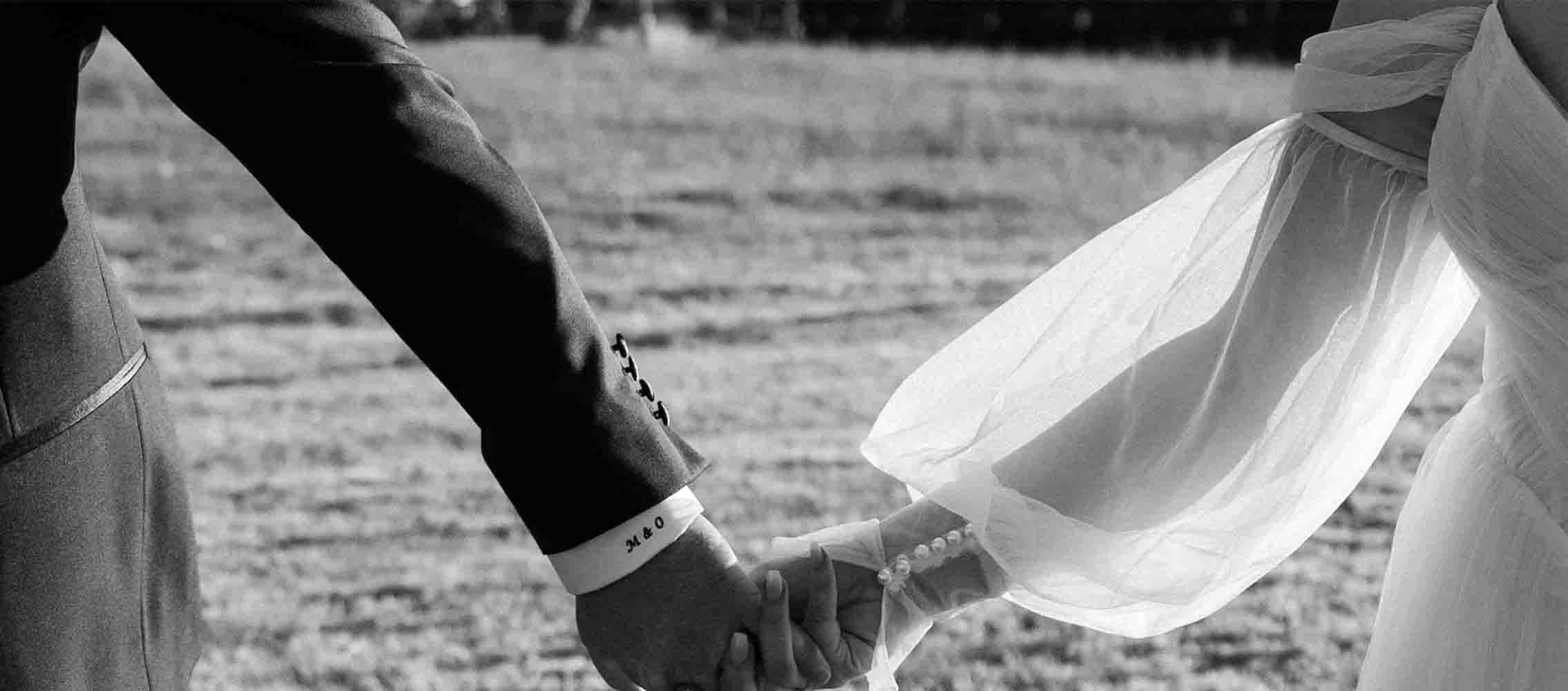 Bride and groom hold hands outdoors, wedding dress flowing, in grayscale photo? (avoid punctuation)