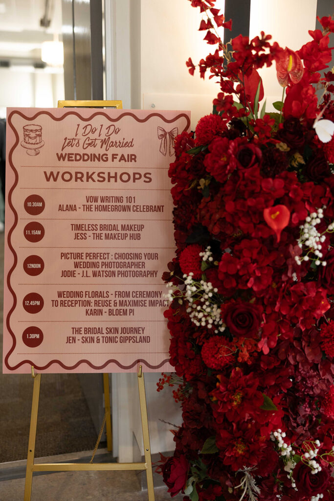 Wedding fair workshop sign with schedule and red floral backdrop; reads 'I Do I Do Lets Get Married WEDDING FAIR WORKSHOPS' and times like 10:30AM, 11:15AM, 12:00PM, etc.