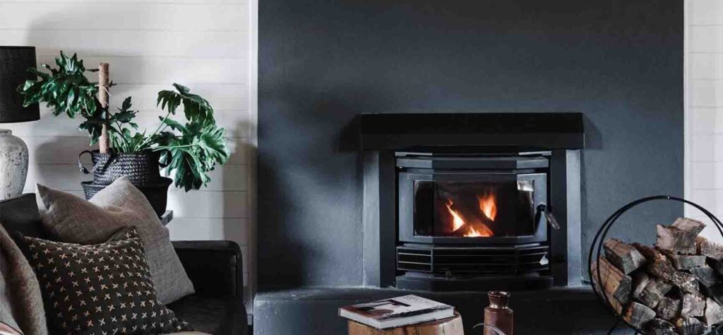 | I do I do Gippsland Cozy living room at The Ridge House with a lit wood-burning fireplace, dark surround, and a sofa with neutral and patterned cushions.