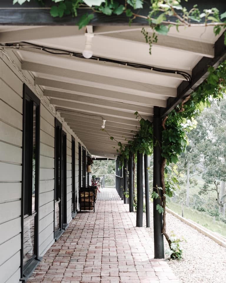 469952147_1292411945442578_5674683176855866414_n | I do I do Gippsland Covered brick-patio walkway along a white house, with black posts and climbing green vines.