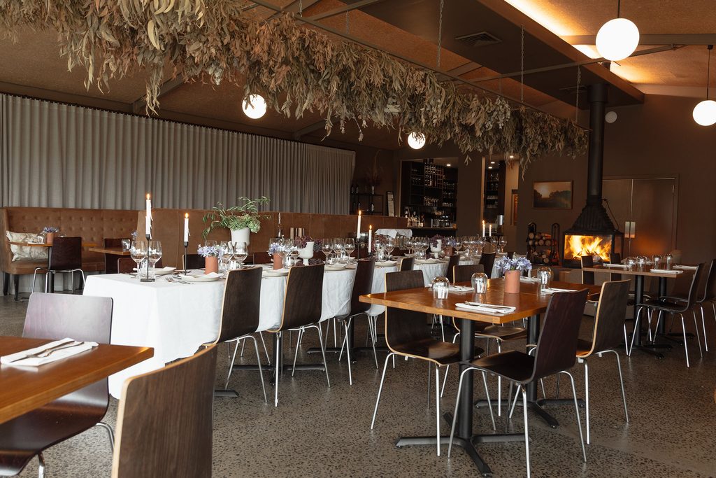 CarrajungEstate_Preview_2026-028 | I do I do Gippsland Banquet hall prepared for dinner with long tables, white tablecloths, candles, and potted flowers; greenery hanging from the ceiling.