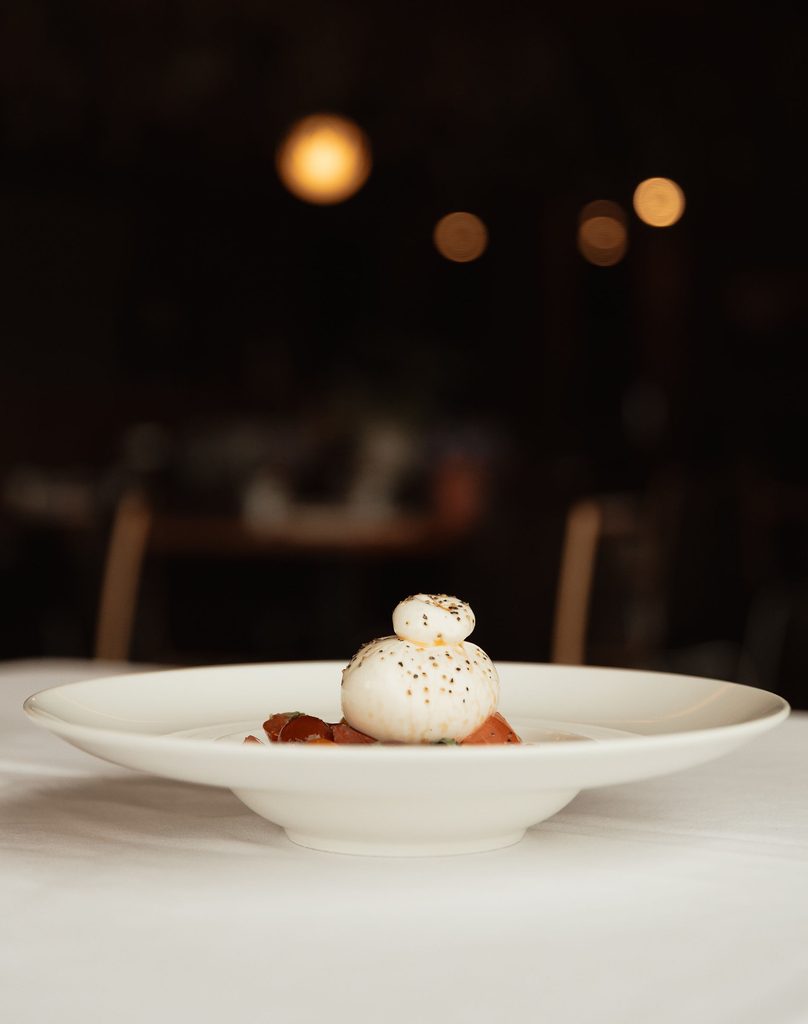 CarrajungEstate_Preview_2026-239 | I do I do Gippsland Stacked small white mushrooms with herbs on a white plate, resting on red sauce, blurred warm lights in the background.