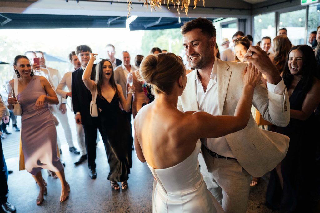 Taylah and Daniel | I do I do Gippsland Couple dancing in the foreground as a cheering wedding guest crowd surrounds them in a bright reception space.
